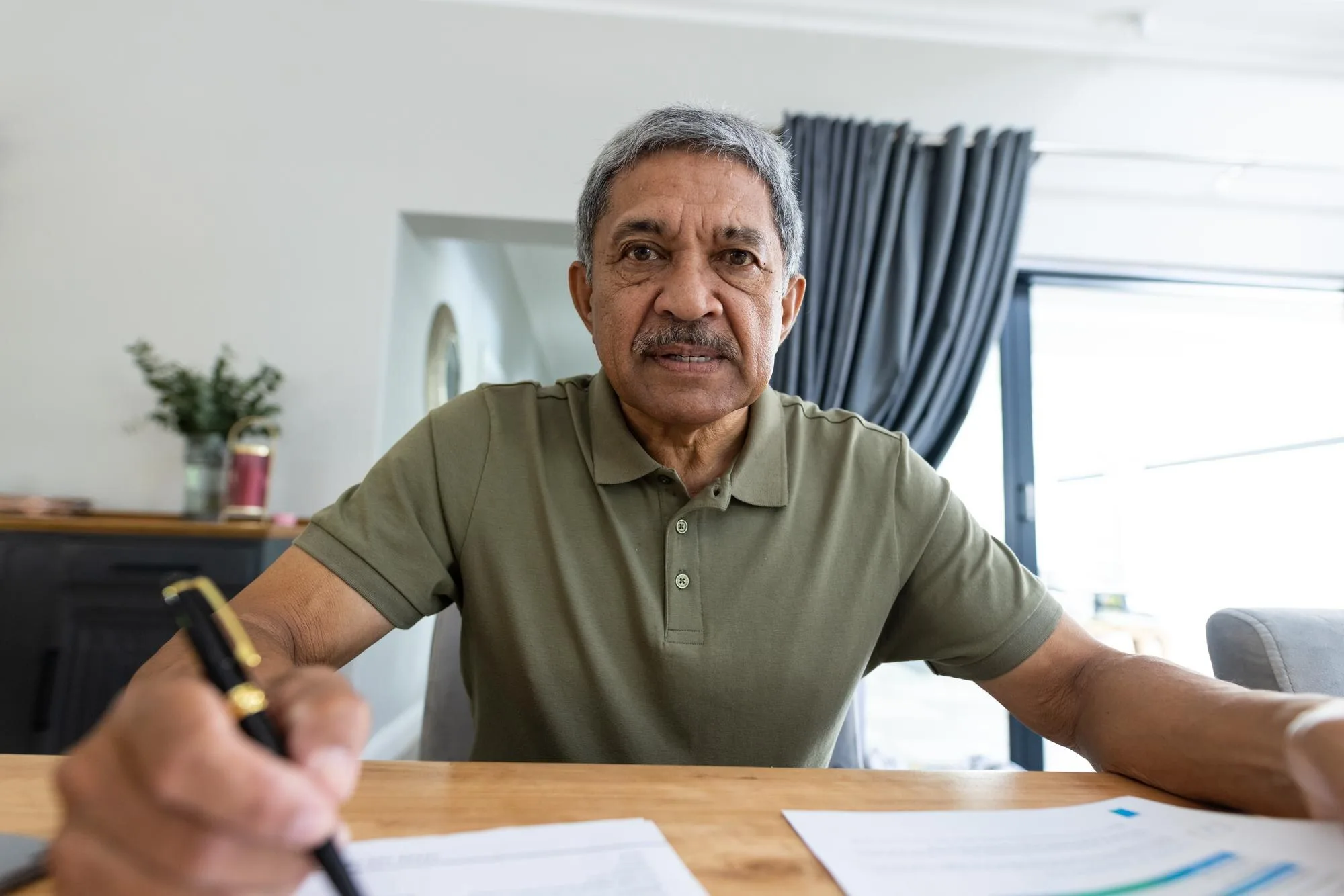 Hombre hispano de mediana edad revisando facturas en mesa de madera para entender el debt settlement