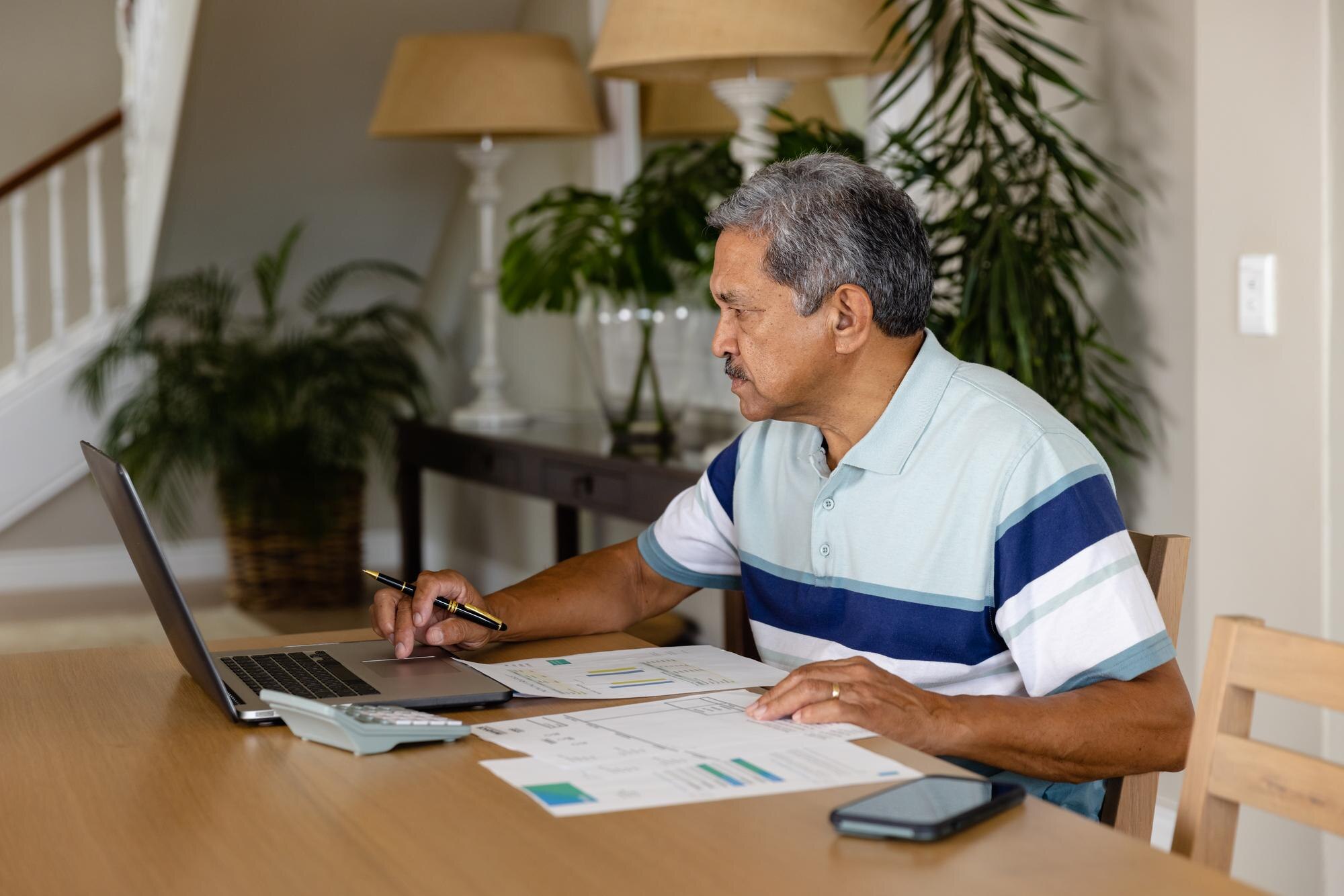 Hombre de mediana edad revisando documentos financieros con laptop en casa - mejorar puntaje de crédito