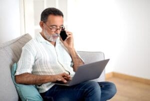 Hombre hispano de mediana edad atendiendo una llamada en su casa mientras detiene llamadas de cobradores de deudas