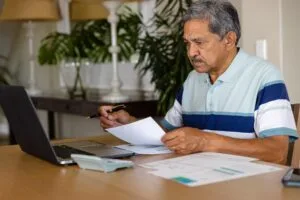 Hombre hispano de mediana edad revisando documentos de consolidación de deuda en su comedor