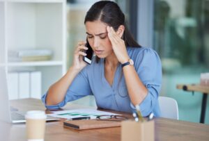 Mujer hispana de mediana edad estresada por llamadas de agencias de cobro sosteniendo su cabeza