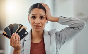 Mujer de mediana edad estresada sosteniendo tarjetas de crédito con expresión de angustia por deudas