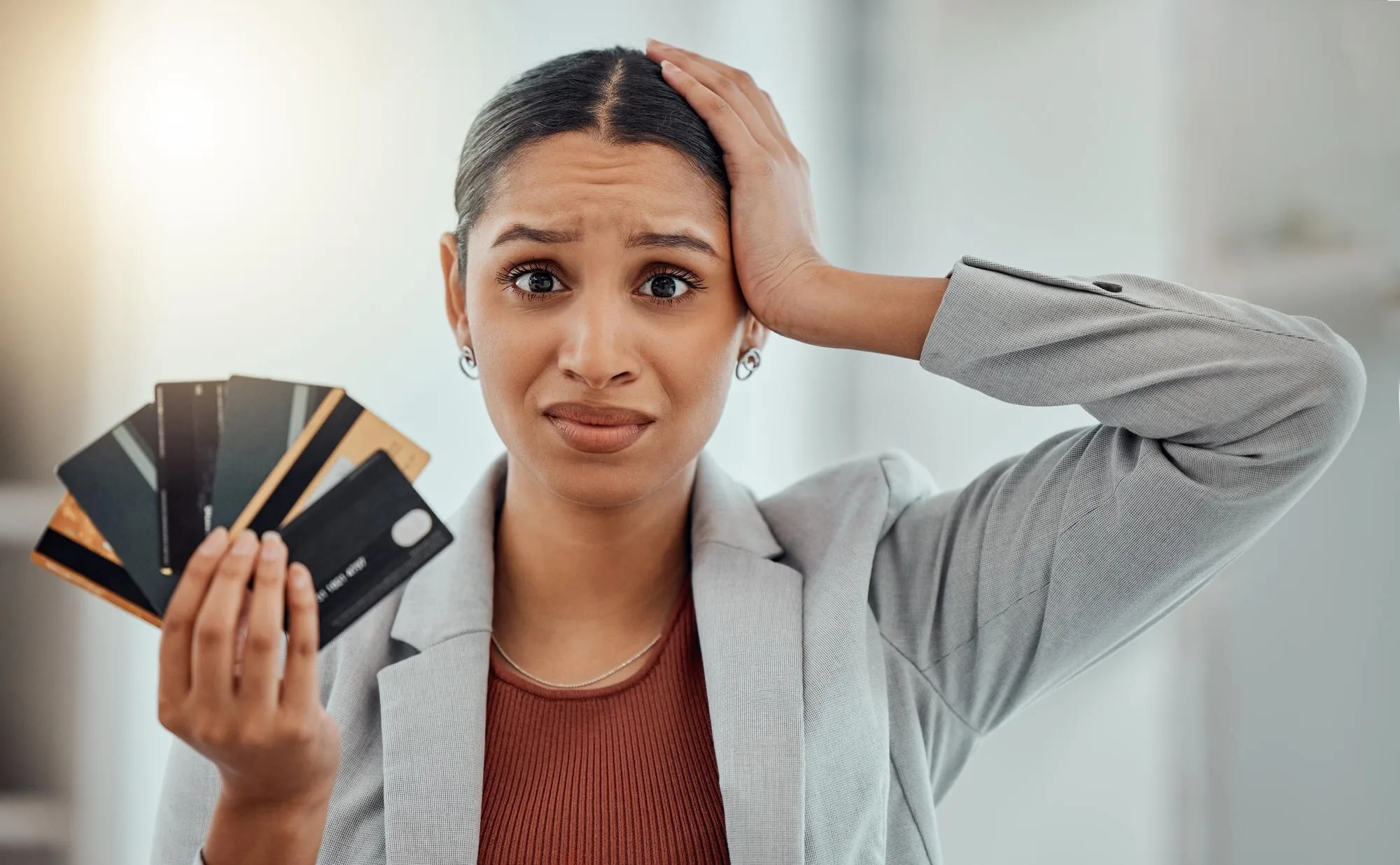Mujer de mediana edad estresada sosteniendo tarjetas de crédito con expresión de angustia por deudas