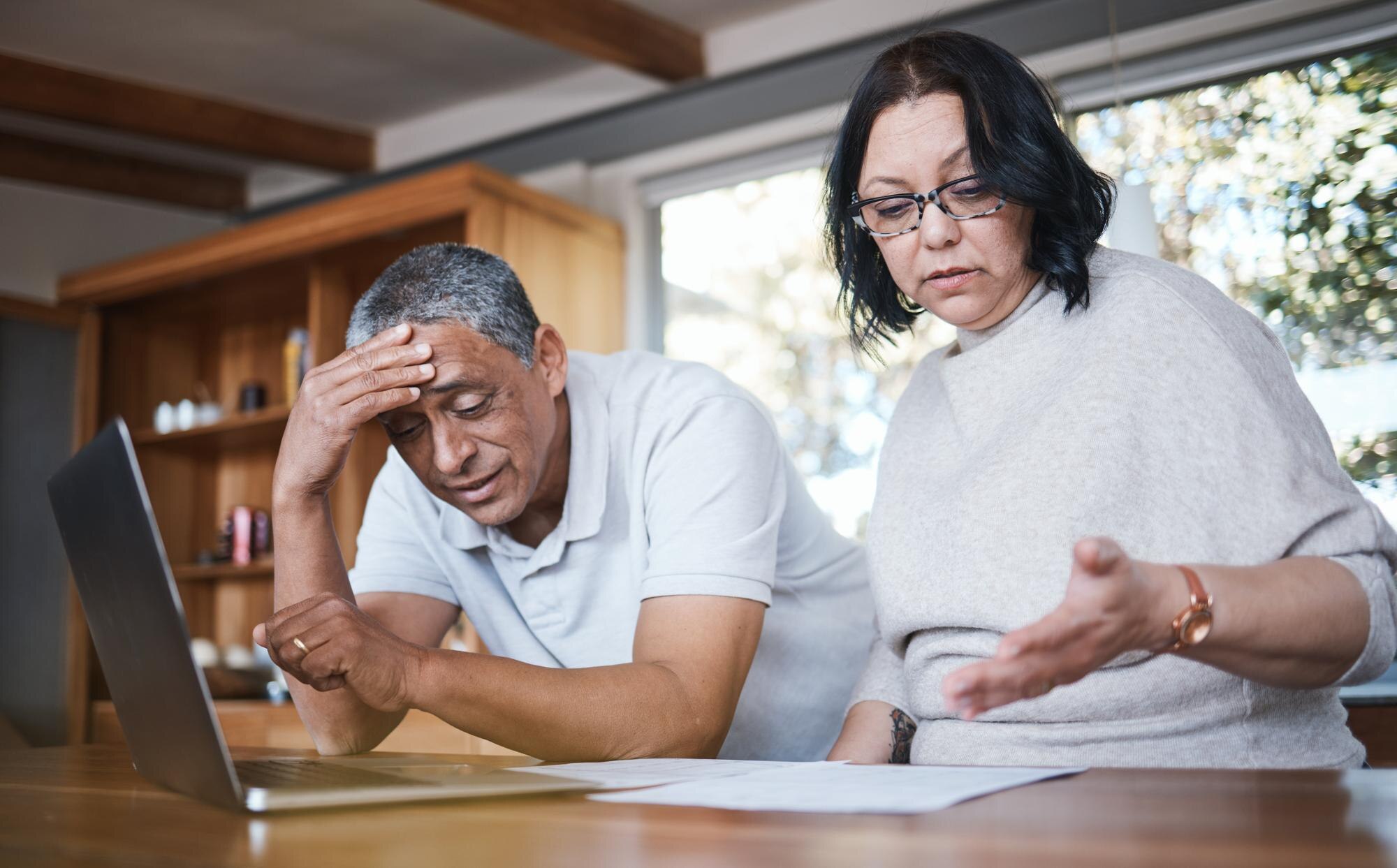 Pareja hispana de mediana edad revisando con preocupación documentos sobre el estatuto de limitaciones de deudas en Estados Unidos
