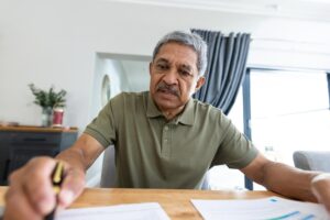 Hombre hispano de mediana edad revisando documentos financieros para solicitar préstamo personal para pagar deudas