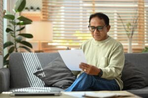 Hombre mayor revisando documentos y reporte de crédito con laptop en sala para entender cuánto tiempo dura una deuda