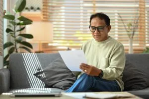 Hombre mayor revisando documentos y reporte de crédito con laptop en sala para entender cuánto tiempo dura una deuda