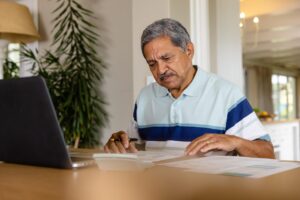 Hombre hispano de mediana edad revisando documentos financieros con laptop — demanda por deuda estados unidos