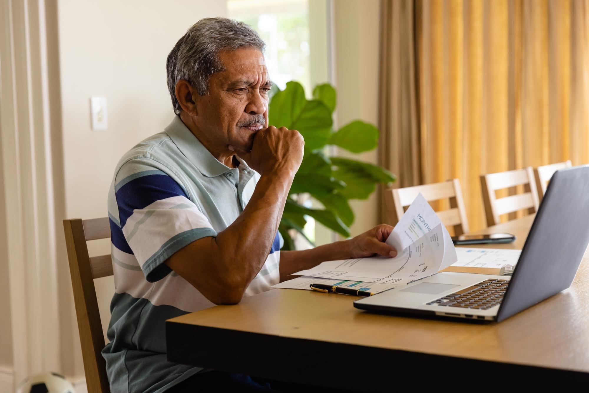 Hombre mayor revisando documentos financieros y laptop - estafas de reparación de crédito