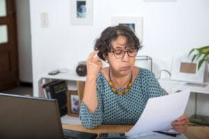 Mujer madura revisando cartas de deudas en colecciones con preocupación en su hogar