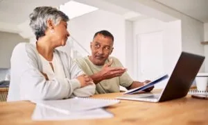 Pareja hispana de mediana edad revisando documentos financieros para calificar al programa de alivio de deudas