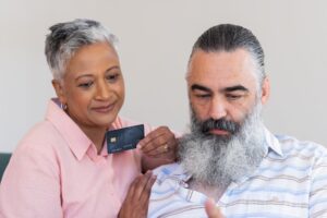 Pareja hispana de mediana edad sosteniendo y revisando tarjeta de crédito asegurada para reconstruir su historial crediticio